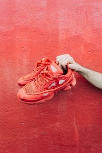 Cropped hand holding shoes against red wall