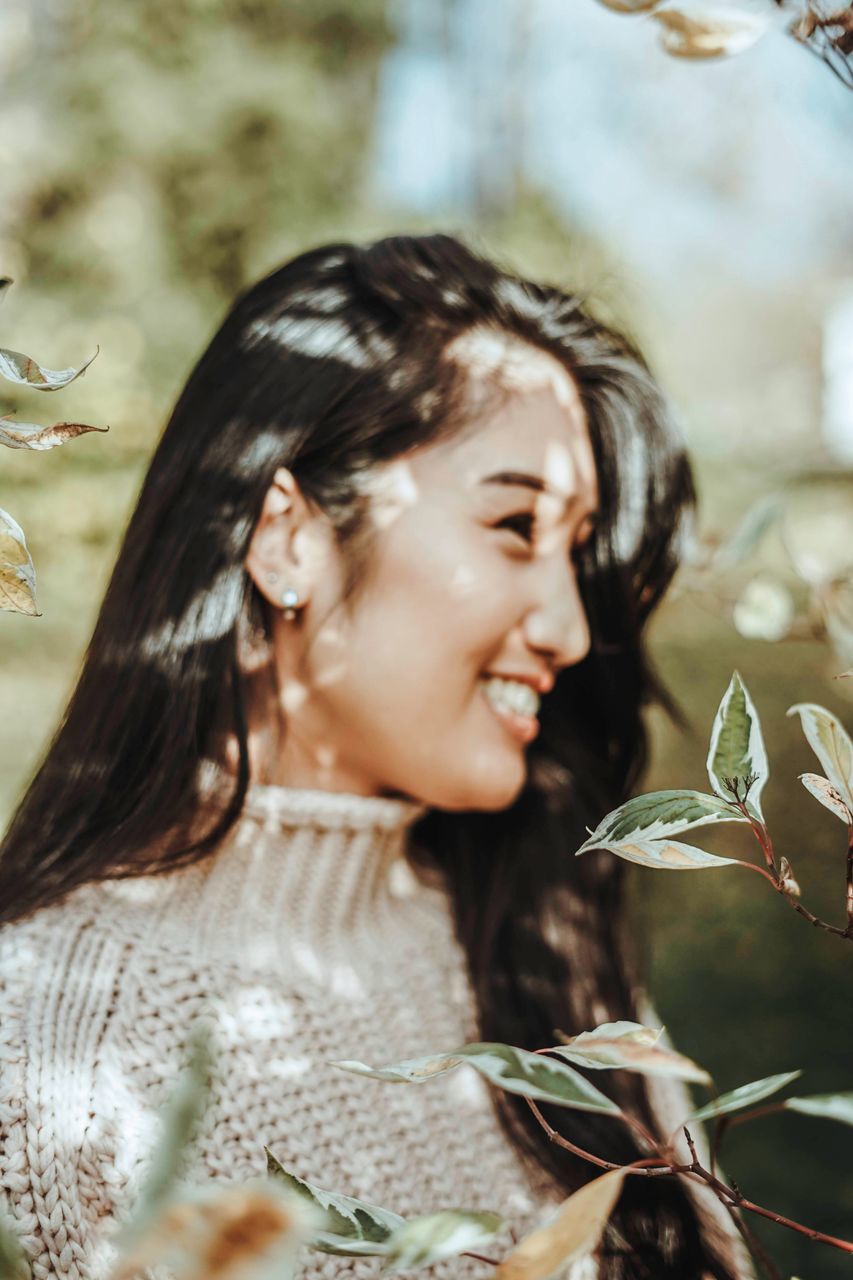 leaf, one person, real people, young adult, plant part, young women, headshot, lifestyles, focus on foreground, women, leisure activity, portrait, nature, plant, smiling, looking, happiness, adult, beautiful woman, hairstyle, outdoors, leaves, contemplation