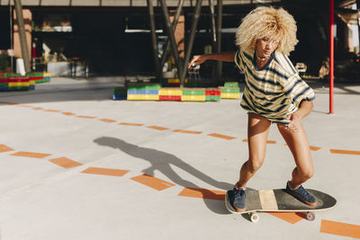 Confident blond woman skateboarding on footpath during sunny day