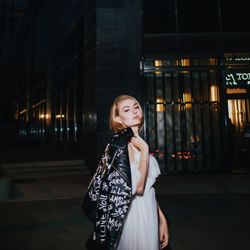 Portrait of young woman standing against illuminated city at night