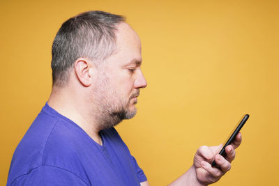 Young man using mobile phone against yellow background