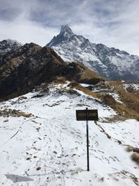 Road sign on snow covered mountain against sky