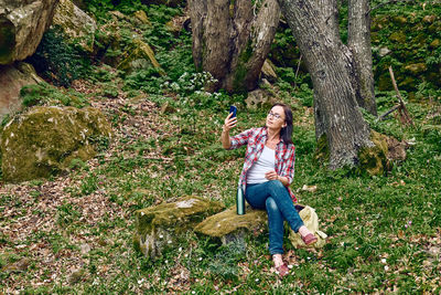 Woman sitting in forest on a stone, using mobile phone for chat or looking for gps. traveling. 