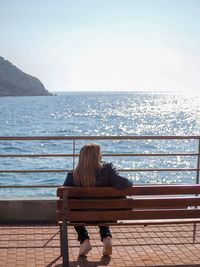 Rear view of woman sitting on bench while looking at sea