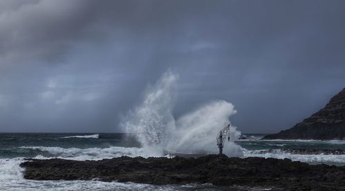 Waves splashing on rocks at shore against sky