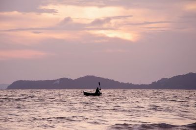 Silhouette man on boat in sea against sky during sunset