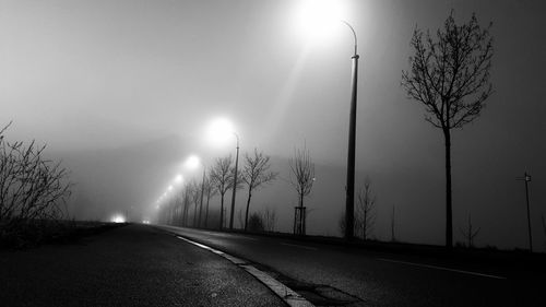 Street amidst trees against sky during foggy weather