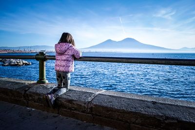 Rear view of woman standing by railing against sea