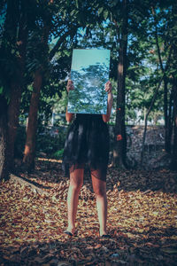 Low section of girl standing on dry leaves while holding mirror
