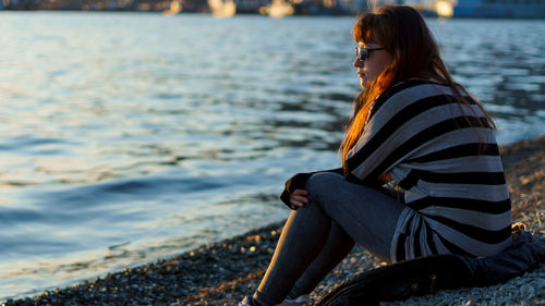 Side view of young woman sitting on shore