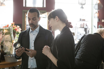 Mature male customer holding magnifying glass while standing by young female entrepreneur at store