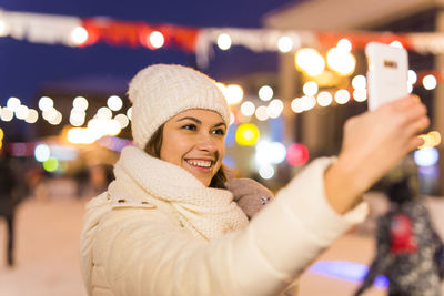 Portrait of smiling young woman in illuminated park during winter