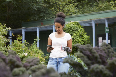 Female gardener using mobile phone amidst plants