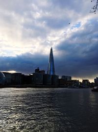 View of buildings by river against cloudy sky