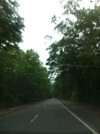 Empty road amidst trees seen through car windshield