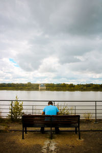 Rear view of man sitting on bench by loire river against sky