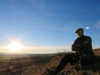 Man sitting on field against sky