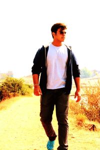 Full length of young man standing on field against clear sky