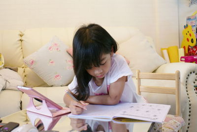 Rear view of girl sitting on book at home