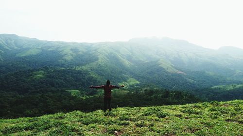 Rear view of man standing with arms outstretched on mountain against sky