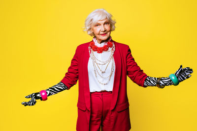 Portrait of senior woman standing against yellow background