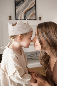 Girl in crown touches nose to nose of her mother holding hands.