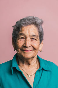 Elderly female with short gray hair and brown eyes looking at camera on pink background in studio