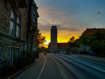 Street amidst buildings against sky during sunset