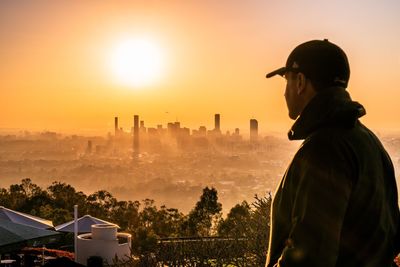 Man standing against cityscape and sky during sunset