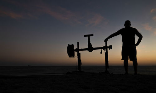 Silhouette man standing on beach against sky during sunset