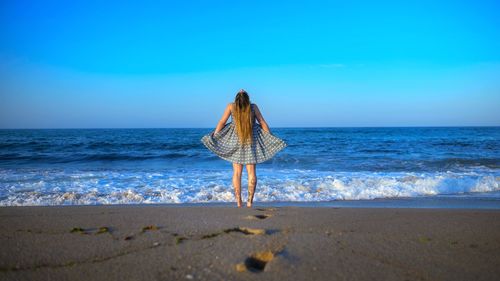 Rear view of woman standing on beach against sky