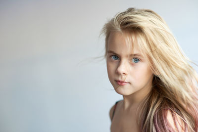 Close-up portrait of girl with blond hair by white background