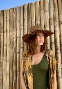 Portrait of beautiful young woman standing against fence