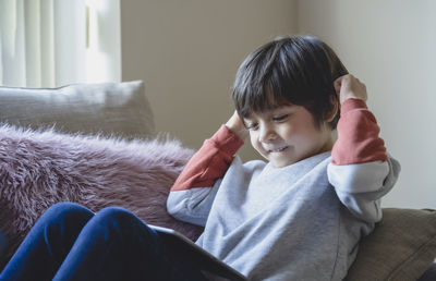 Smiling boy looking at digital tablet while sitting on sofa