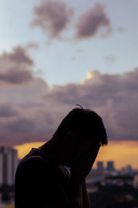 Silhouette of crying depressed man with cloud sky and city background.