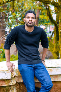 Portrait of young man sitting against trees