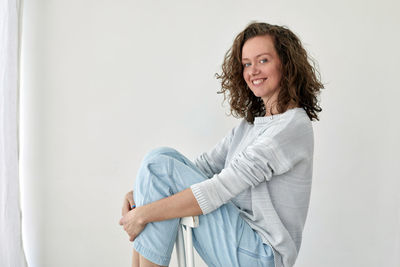 Portrait of a smiling young woman standing against wall