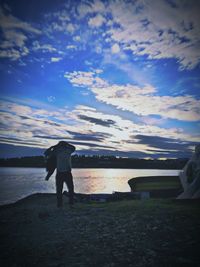 Rear view of man standing on beach against sky during sunset