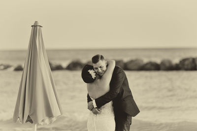 Happy groom embracing bride at beach