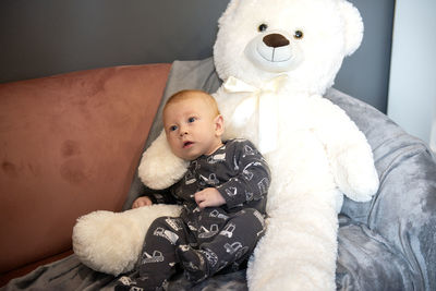 Smiling newborn baby and big white teddy bear sitting on sofa or couch