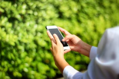Cropped hands of woman using mobile phone against plants