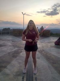 Portrait of smiling young woman standing against sky during sunset