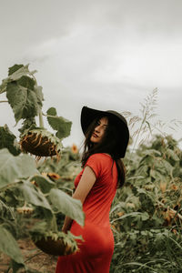 Young woman standing amidst sunflowers on field against sky