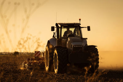 Tractor on field against sky during sunset