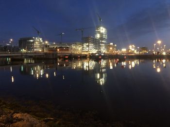 Illuminated city by river against sky at night