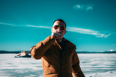 Portrait of young man wearing sunglasses standing against sea