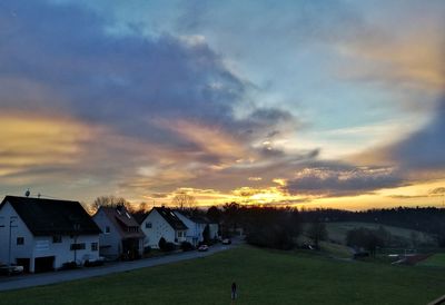 Houses by trees against sky during sunset