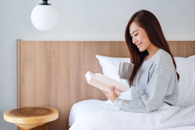 Portrait of young woman using mobile phone while sitting on bed at home