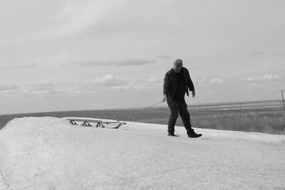 Man with sled on snowy field against sky