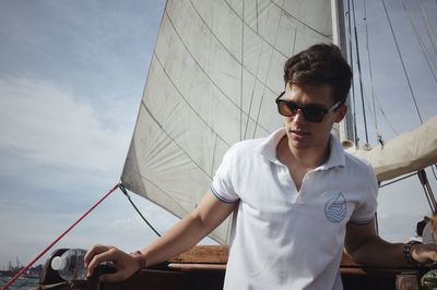 Young woman wearing sunglasses standing by boat against sky